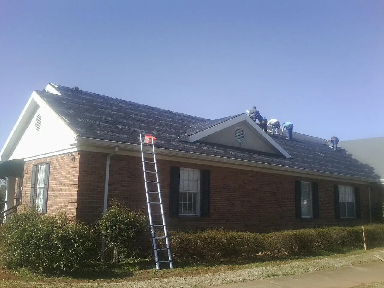 Crew tearing shingles off a brick ranch roof with a ladder set — Metal Roof Repair work by our crew in Rock Tavern