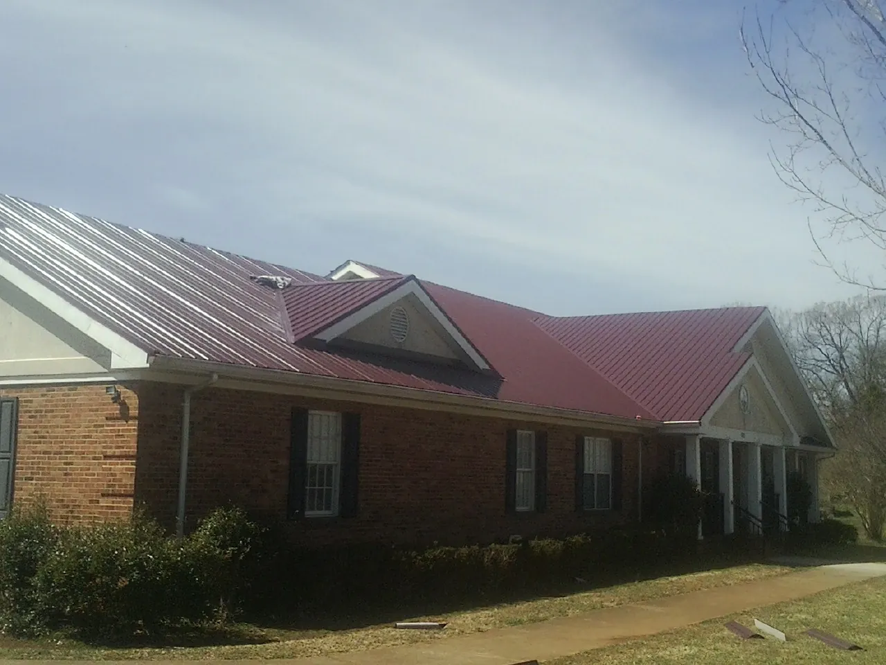 Red metal roof with gabled entries on a long brick building, from a Hail Damage Roof Repair job in Rock Tavern
