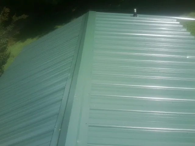 New green metal panels meeting at the ridge of a roof — Flat Roof Repair work by our crew in Rock Tavern