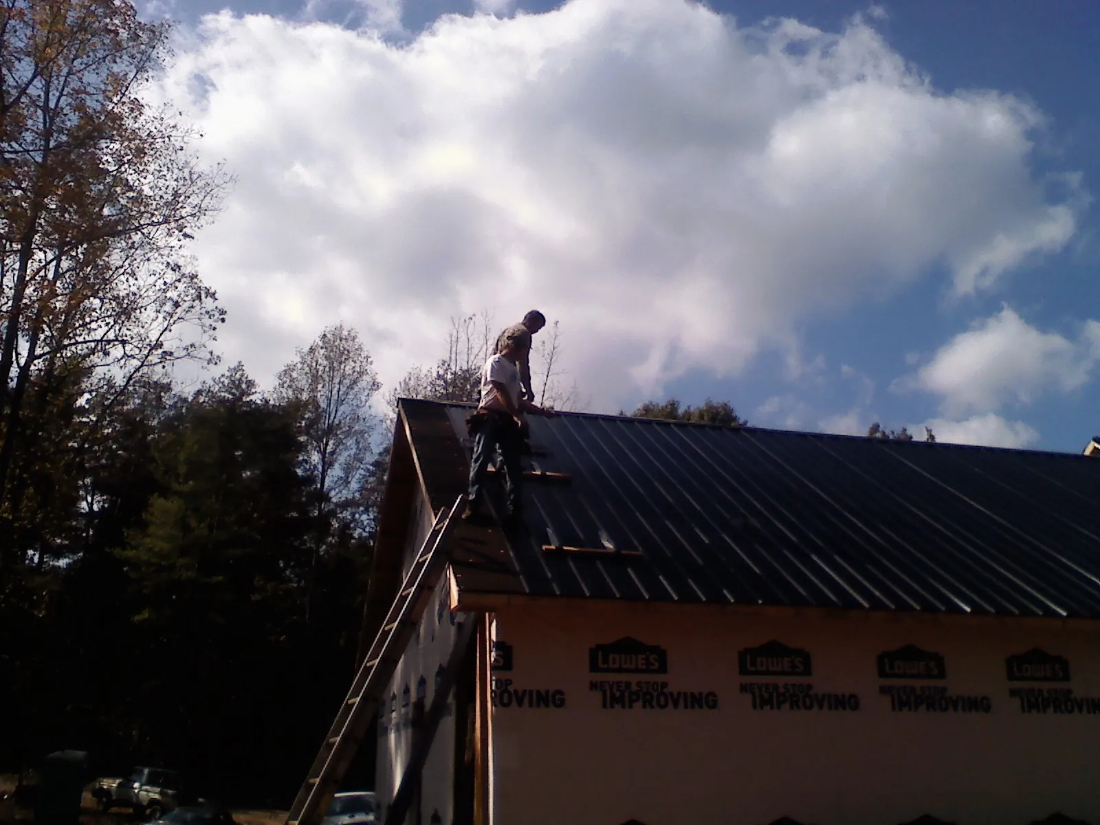 Roofer fastening dark metal panels high against a cloudy sky, from a Roof Inspection job in Rock Tavern