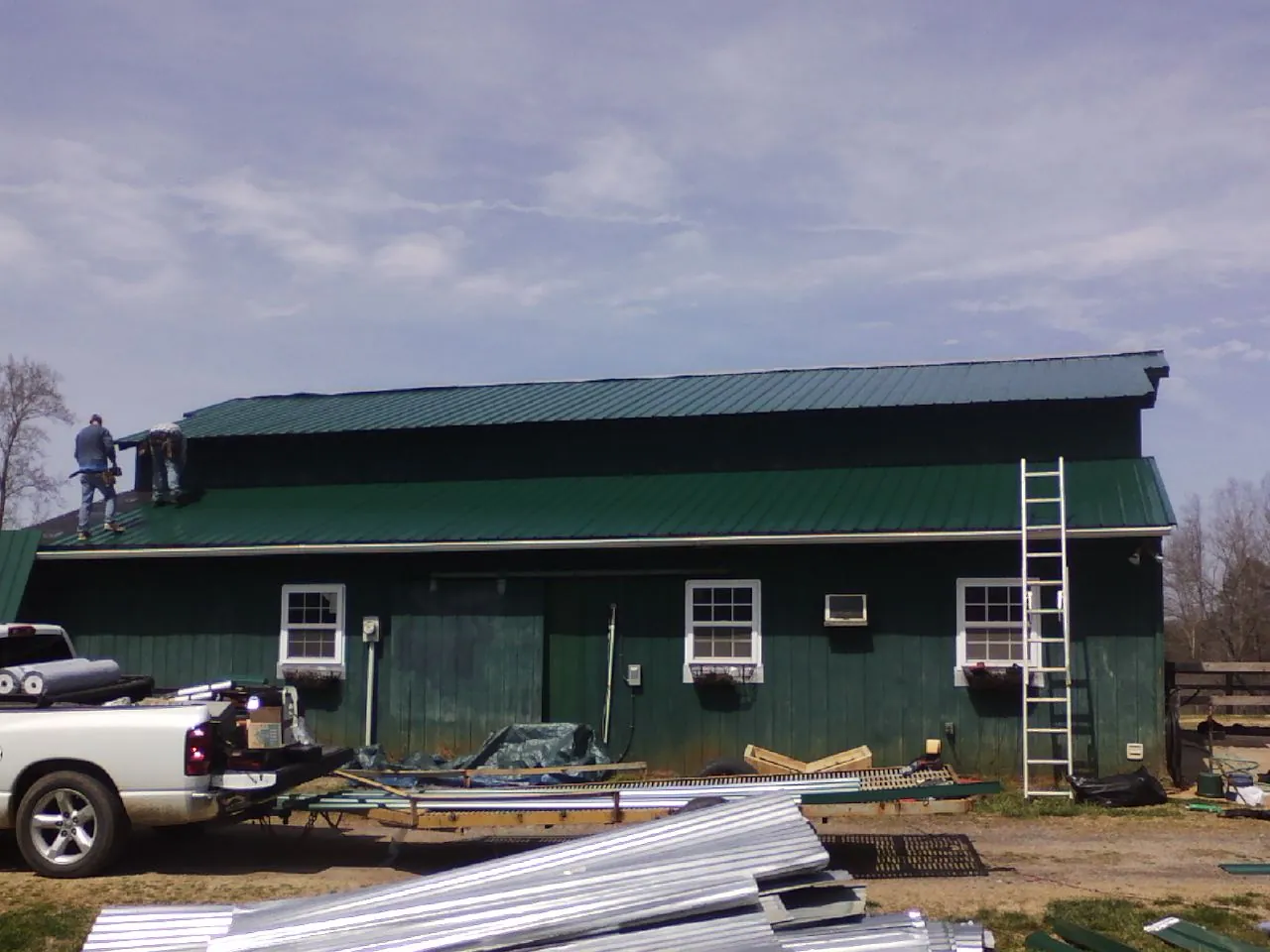 Crew installing green metal roofing on a large green barn in Rock Tavern