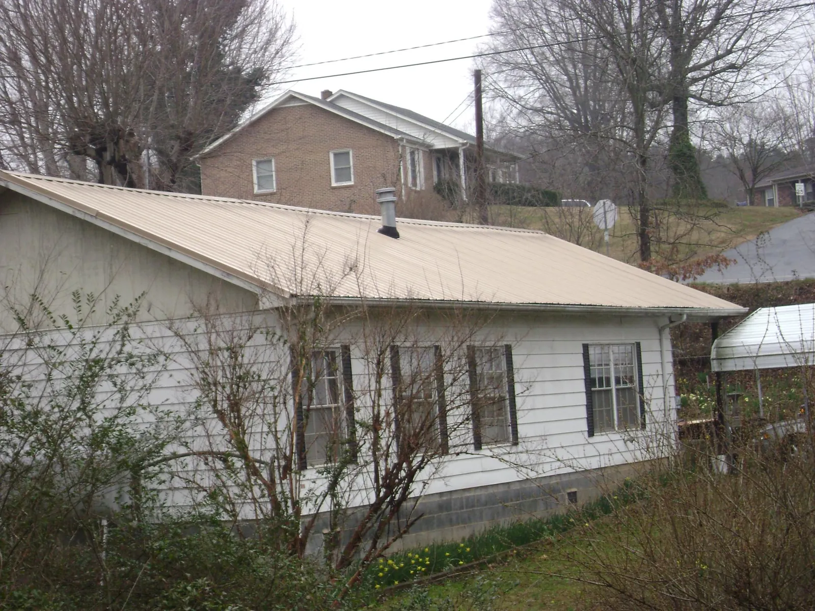 Tan metal roof on a white sided house set into a hillside — Commercial Roofing by Roofing Brothers in Rock Tavern